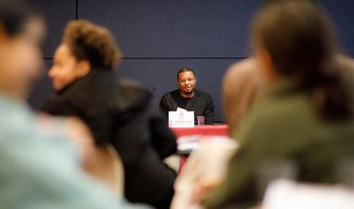 A man sits at the front of the room with students listening to him talk 